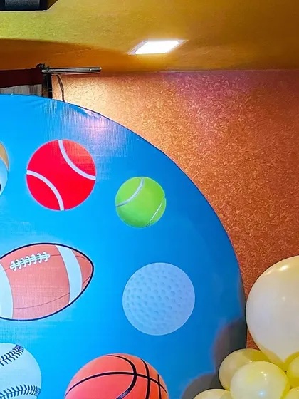 A sports-themed backdrop featuring graphics of a volleyball, tennis ball, football, and more.