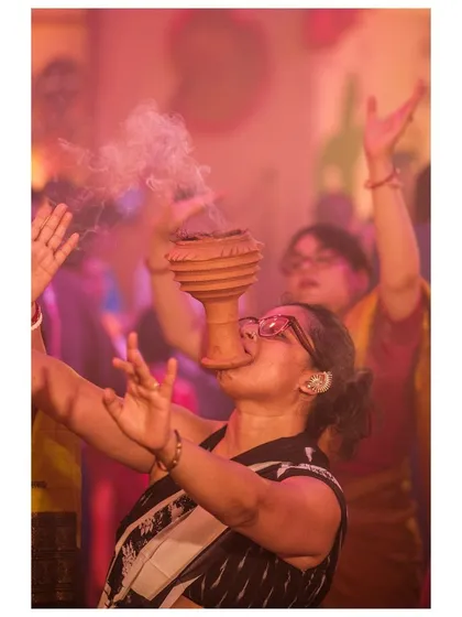 A devotee raises her hands in prayer while balancing the dhunuchi, a moment of intense spiritual focus.