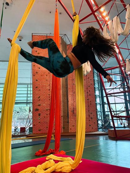 A dynamic spinning pose on the yellow silks, capturing the fluid motion and excitement of aerial dance.