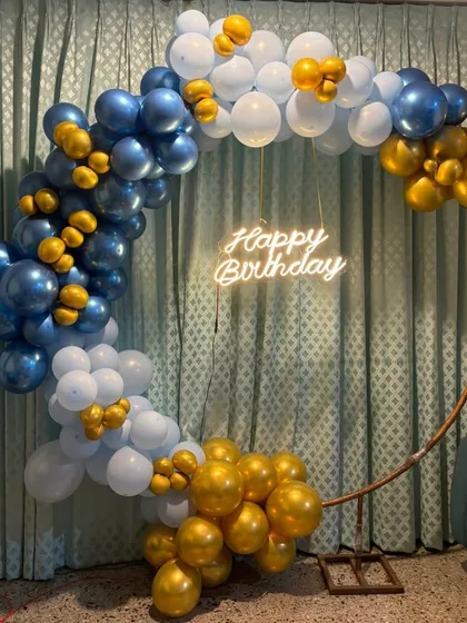 Our classic ring garlands are perfect for any occasion. This design features a stylish half-arch of royal blue, white, and gold chrome balloons on a copper-colored ring, finished with a 'Happy Birthday' neon sign for a clean and celebratory look.