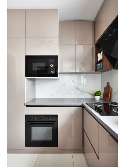 This compact kitchen is designed for maximum efficiency. It features glossy beige acrylic cabinets, a built-in oven and microwave tower, and a durable grey quartz countertop that extends up into a seamless backsplash.