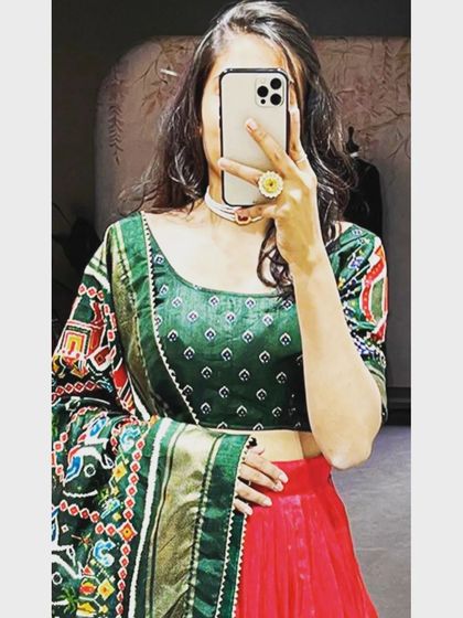 A close-up mirror selfie of the green and red art silk lehenga. This view details the print on the blouse and the heavy, traditional weave of the Patola-style dupatta.