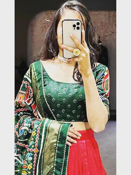 A close-up mirror selfie of the green and red art silk lehenga. This view details the print on the blouse and the heavy, traditional weave of the Patola-style dupatta.