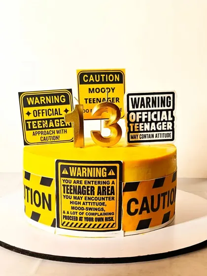 "Warning: Official Teenager." A fun and bold cake for a 13th birthday, designed to look like yellow caution tape with humorous warning signs.