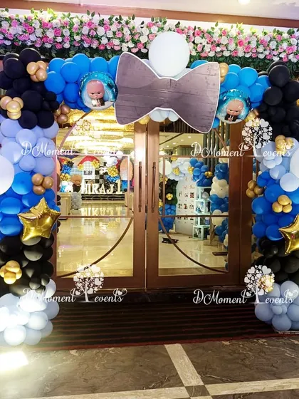 A grand entrance arch for the Boss Baby party, complete with a large bowtie prop and columns of blue, black, and white balloons.