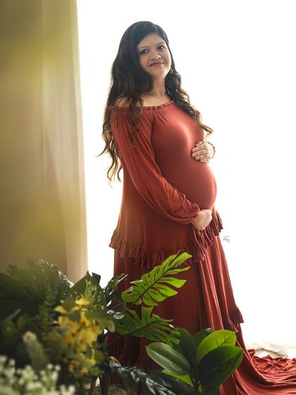 A bright and happy portrait. The mother-to-be's smile shines in this light-filled image, framed by soft greenery.