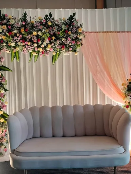 An elegant L-shaped floral arch framing a modern sofa. This asymmetrical design is perfect for a contemporary engagement or reception stage.