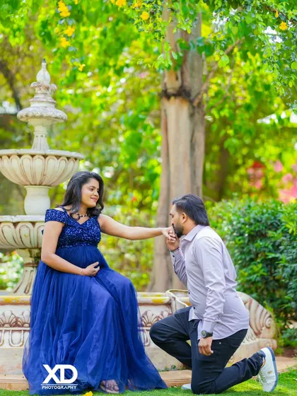 A chivalrous and romantic pose with the partner kneeling to kiss the mother-to-be's hand by a garden fountain.