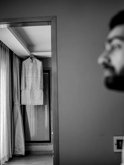 A thoughtful black and white shot of the groom looking towards his wedding sherwani. This image captures the anticipation and quiet moments before he gets ready.