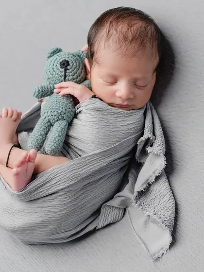 A perfectly swaddled newborn cuddling a tiny teddy bear. Using simple props and a neutral grey backdrop keeps the focus entirely on your baby's peaceful expression and tiny features.