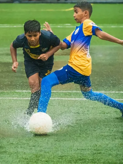 A U13 player shows great technique, kicking the ball through the water in a challenging monsoon game.