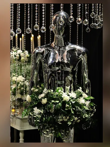 A close-up of a chrome mannequin holding a bouquet of white flowers, under a curtain of hanging crystals.