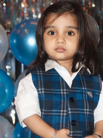 A close-up portrait of a young boy in a smart plaid vest, looking intently at the camera.