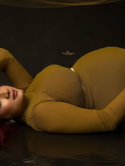 A unique and artistic pose from a modern maternity session. The mother-to-be lies gracefully on a reflective floor, creating a stunning and unconventional portrait.
