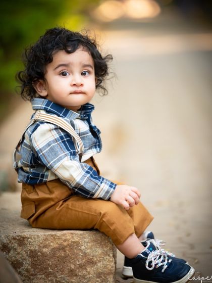 A sweet, thoughtful portrait of a toddler boy sitting on a rock. The soft, natural background keeps the focus entirely on him.