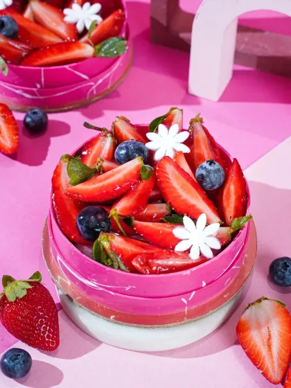 A vibrant strawberry and blueberry dessert in a pink marbled chocolate shell. The bright pink background and scattered berries create a fresh and modern look.