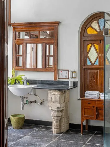 The bathroom in the Arundati suite features a modern glass shower enclosure next to a traditional stained-glass window, a perfect mix of old and new.