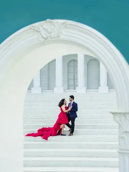 A dramatic and elegant portrait on a grand white staircase. The bride's flowing red gown creates a stunning visual contrast against the pristine architecture, making for a truly show-stopping image.