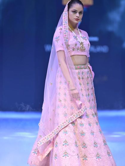 A side view of the pastel pink lehenga, showing the flow of the skirt and the beautifully detailed belt. The look is completed with a sheer dupatta and traditional jewelry.
