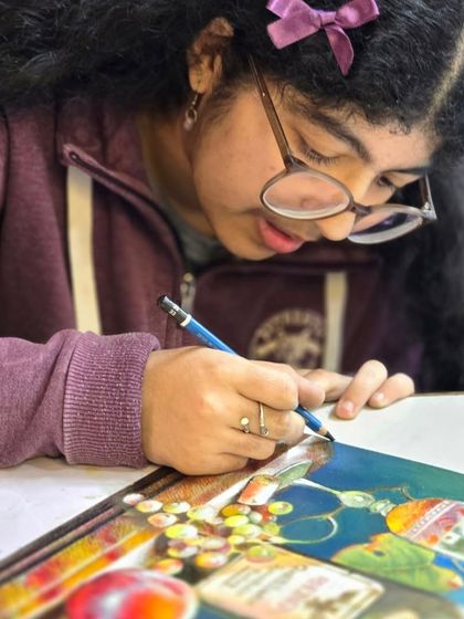 A close-up of the student's hands at work, showing her technique for blending and layering oil pastels to create realistic textures and colors.