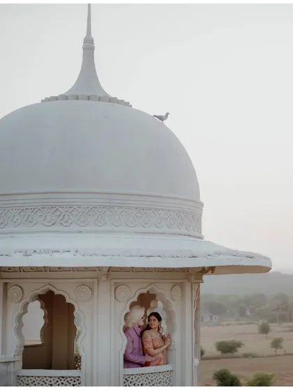A fairytale view from a palace turret in Jaipur. The couple shares a quiet moment, framed by the window, with a lone bird perched on the dome, adding a touch of serendipity to this romantic pre-wedding scene.