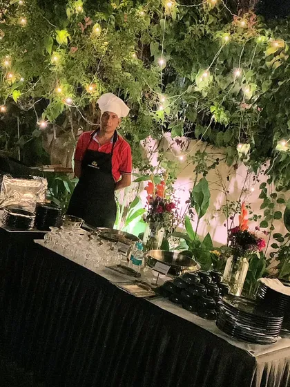 A member of my culinary team at a live counter during an outdoor event. Dressed in professional chef's attire, they are ready to serve fresh and delicious food under the stars.