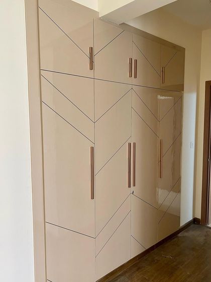 A large, four-shutter wardrobe in a high-gloss beige finish with a modern geometric pattern and rose-gold handles.