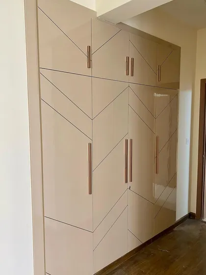 A large, four-shutter wardrobe in a high-gloss beige finish with a modern geometric pattern and rose-gold handles.