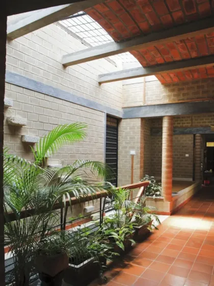 The sunlit corridor of Mr. Petachi's house, featuring exposed brick walls and a skylight. The row of indoor plants adds life and freshness, demonstrating how even transitional spaces can be designed to connect with nature.