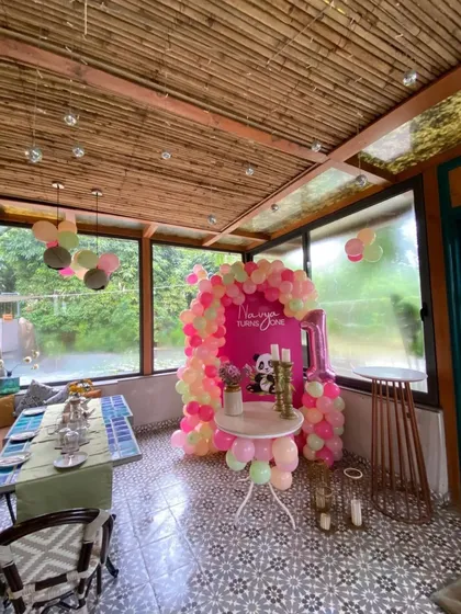 A sweet panda-themed first birthday. This setup in a restaurant space includes a pink backdrop with a cute panda, a personalized message, and a matching balloon arch.