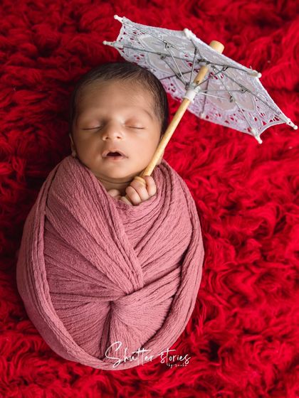 A creative portrait using a miniature lace umbrella as a prop. The rich red background makes the baby and the prop stand out.