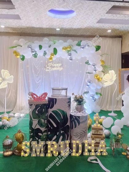 A nature-inspired birthday theme with a white and green balloon arch, leaf-printed props, and glowing flower lights.