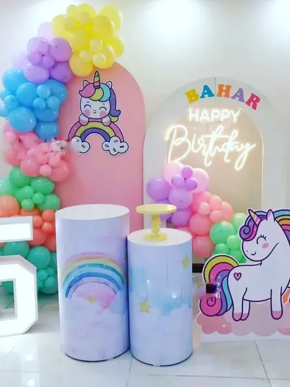 A magical unicorn and rainbow theme for a fifth birthday. The decor uses pastel colors, a neon sign, and cute unicorn cutouts.
