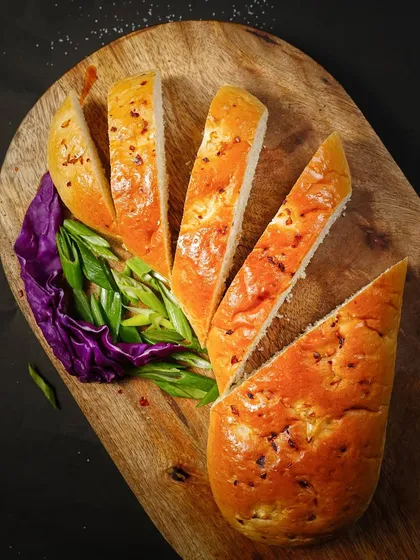 An overhead shot of sliced garlic bread arranged艺术fully on a wooden board. The dark background makes the warm colors of the bread pop.