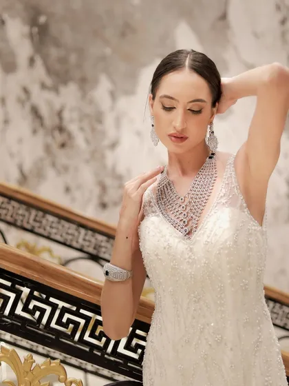 A high-fashion pose from a modeling shoot, with the model showcasing an elegant white gown and dazzling diamond jewelry set against a marble staircase.