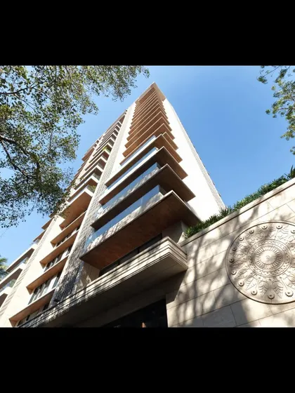 An upward perspective of the Supreme Universal tower, showcasing the detailed stonework and the interplay of light and shadow on the facade. The design incorporates a traditional motif, blending modern architecture with artistic details.