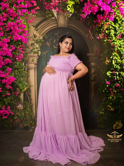 A joyful and radiant portrait of the mother-to-be in a lavender gown, surrounded by vibrant pink bougainvillea in a studio setup.