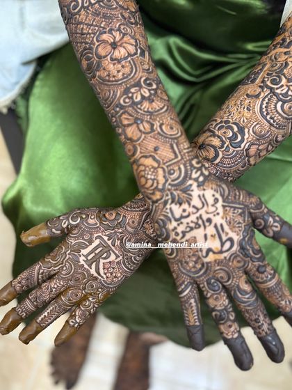 A beautiful angled shot showing the groom's initial 'R' and an Arabic phrase as the centerpiece of the palm designs.