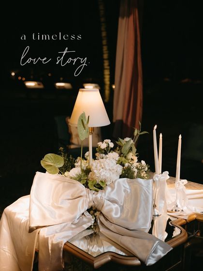 A table centerpiece with a lamp and a large silver bow, with the text overlay "a timeless love story".