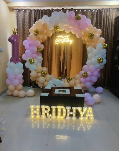 A chic first birthday decoration for a home setting, with a pastel balloon ring, a neon sign, and a large number '1' foil balloon.