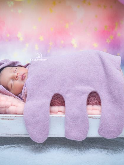 A soft and dreamy portrait with a baby sleeping under a purple elephant-shaped blanket against a pastel rainbow background.
