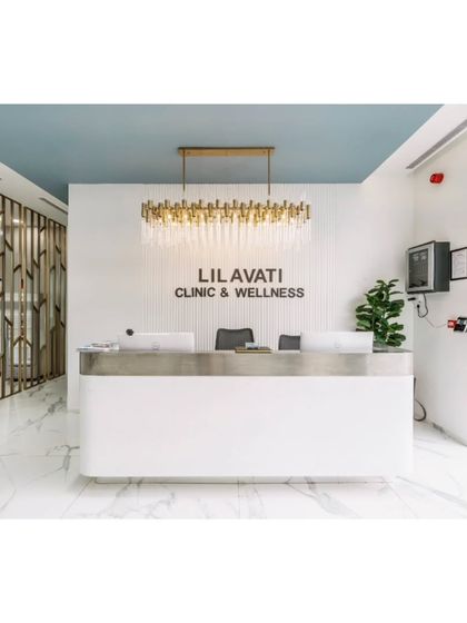 The main reception desk at the Lilavati Clinic and Wellness center features a stunning chandelier and a clean, white counter. The design is intended to be welcoming and professional, with a decorative metal screen adding a touch of elegance.