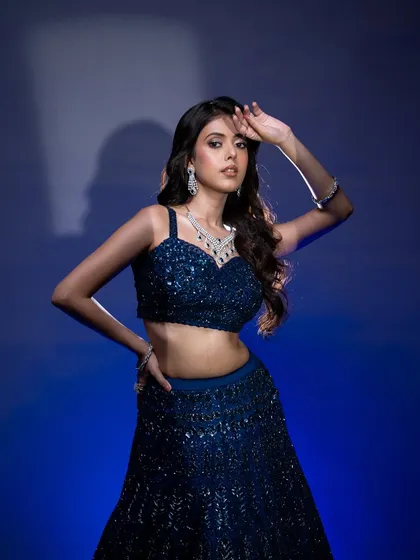 A stunning reception or cocktail look featuring a deep blue sequined lehenga. The makeup is glamorous with a defined eye, contoured cheeks, and a neutral lip.