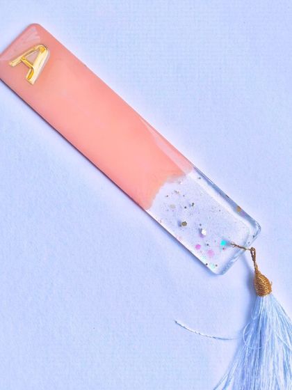 A flat-lay photo of the pastel pink initial bookmark, showing the full design and the light blue tassel.