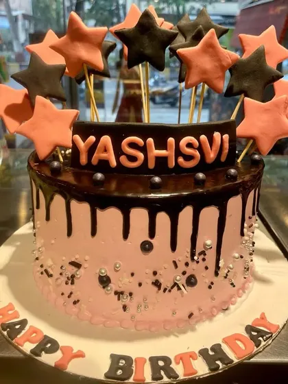 A stylish pink and black drip cake perfect for a chic birthday celebration. This cake is topped with a burst of pink and black stars and features a rich chocolate drip over light pink frosting.