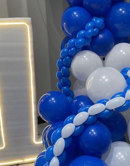 A close-up of the decor for the corporate anniversary, showing the "1" LED number next to a cascade of blue and white balloons, with a Ganesha idol for blessings on the milestone.