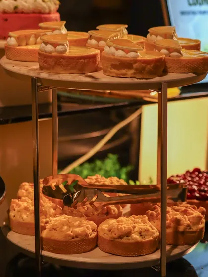 A two-tiered stand filled with delicious pastries, including lemon meringue tarts on top and apple crumbles on the bottom.