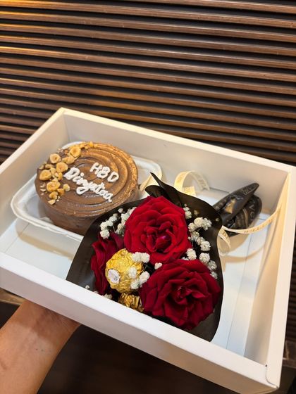 This birthday hamper features a delicious chocolate bento cake topped with hazelnuts, paired with a mini bouquet of red roses and Ferrero Rocher. It's a classic combination for a special celebration.