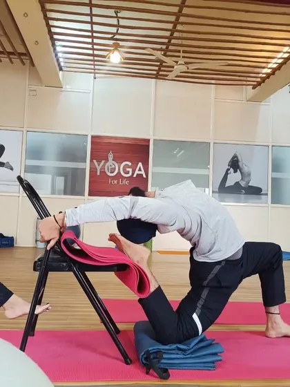 A student practices a supported backbend using a chair. This demonstrates how props can be used to work towards more advanced poses like Kapotasana (Pigeon Pose) safely and effectively.