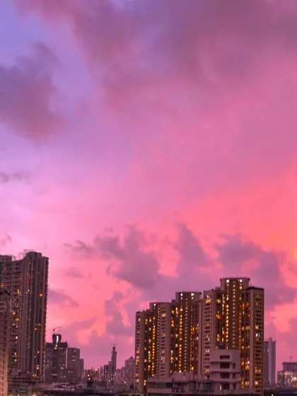 The sky above Mumbai is a brilliant magenta and purple during sunset, with the city's buildings lit up against the colorful display.